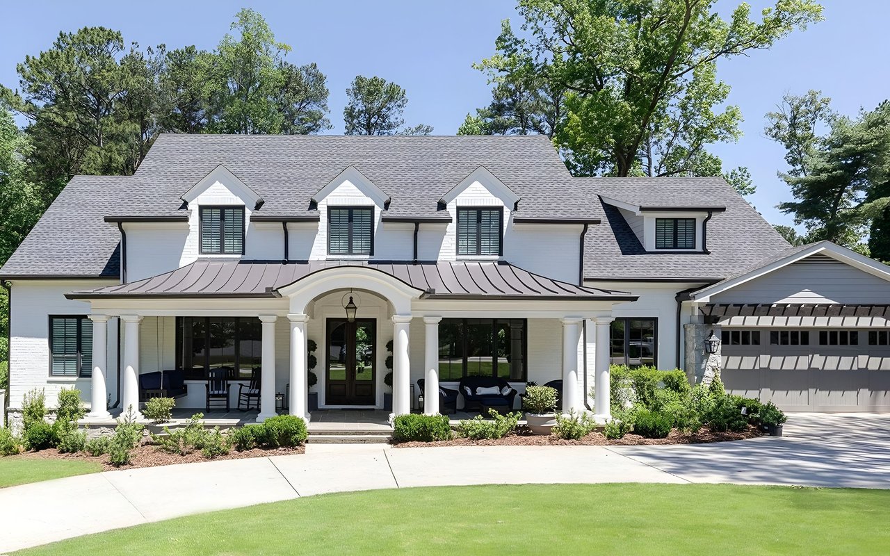White two-story house with three dormers, a columned porch, and an attached garage.