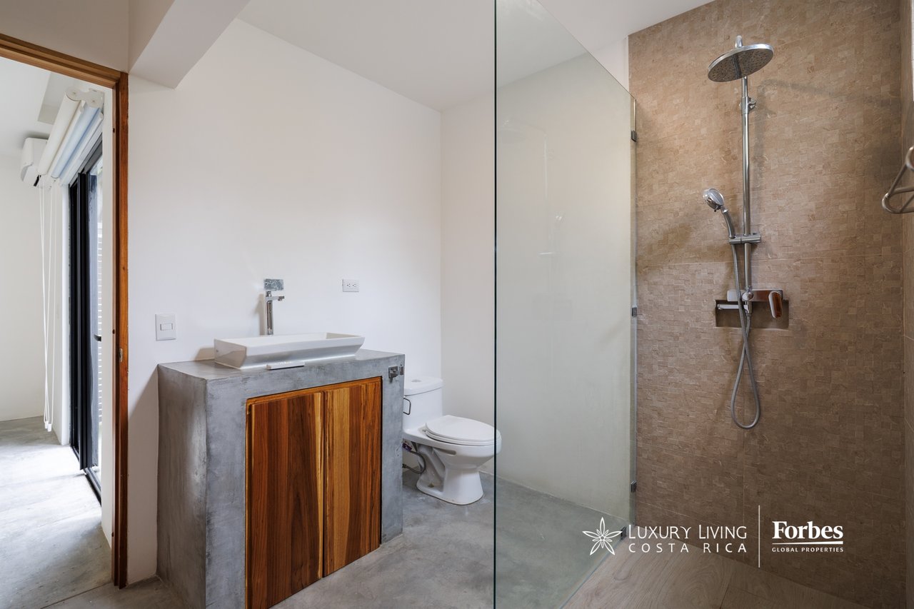 Modern bathroom with a stone-tiled glass shower and concrete vanity with wooden cabinet doors.