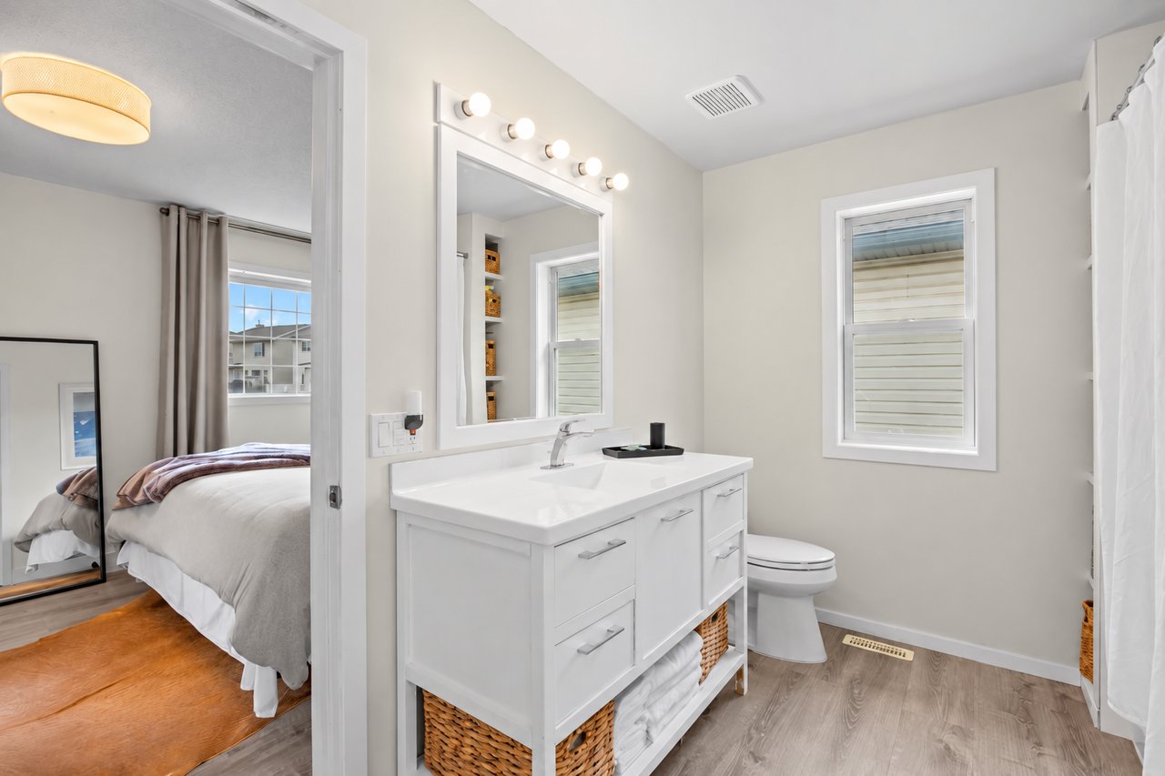Bathroom with a white double vanity, large mirror, toilet, and shower curtain beside a bedroom.