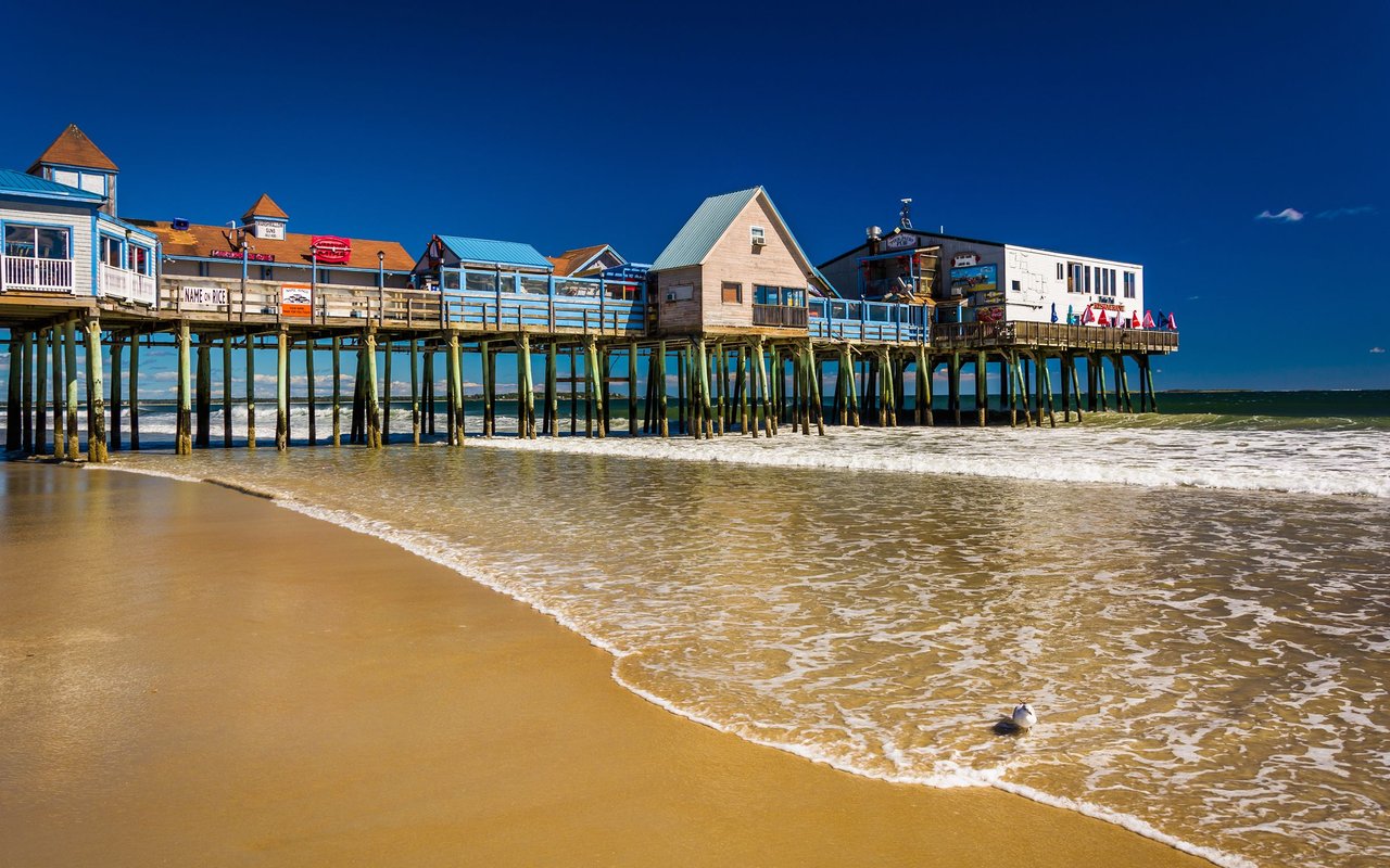 Old Orchard Beach pier extends over the ocean beside a sandy beach.