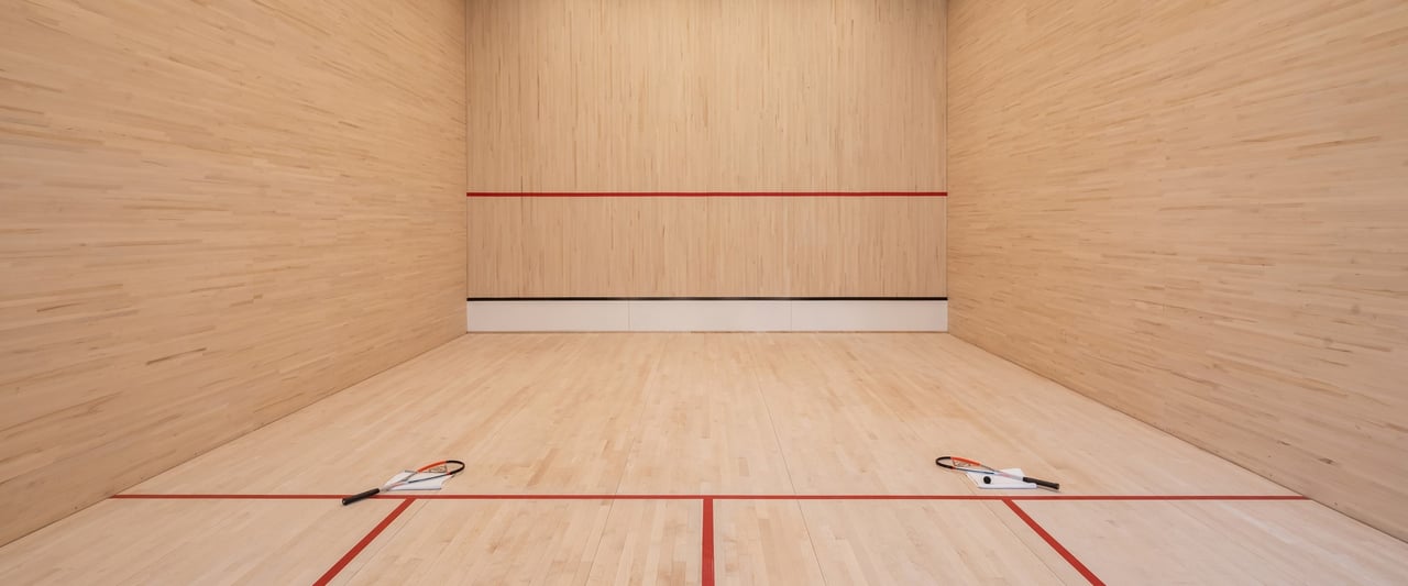 Wood-paneled squash court with red court lines and two rackets.