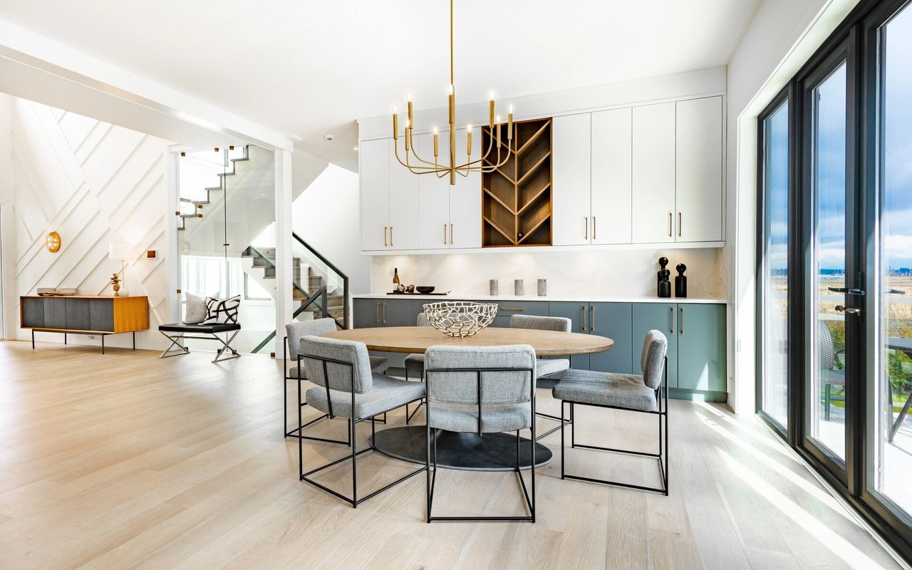 Dining area with a round wood table, gray chairs, built-in cabinetry, and a staircase beside glass doors.