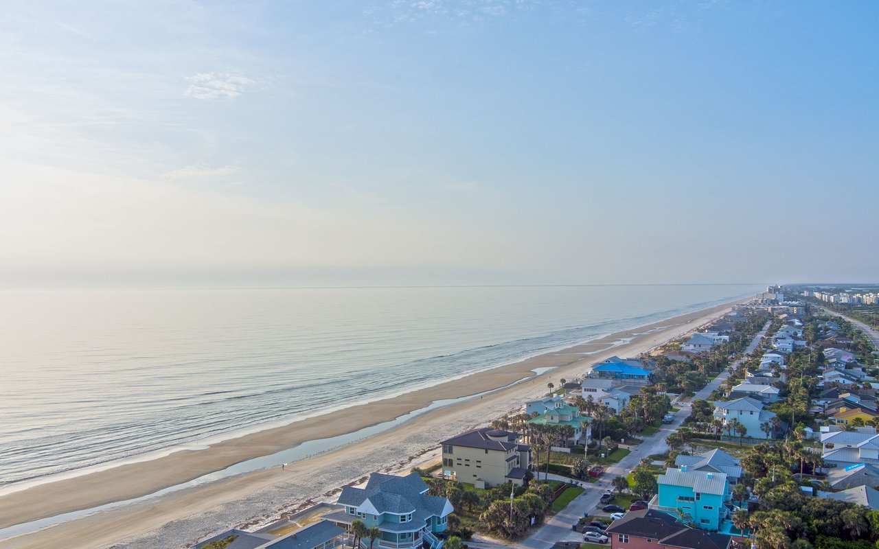 Aerial view of coastal homes beside a long sandy beach and calm ocean.