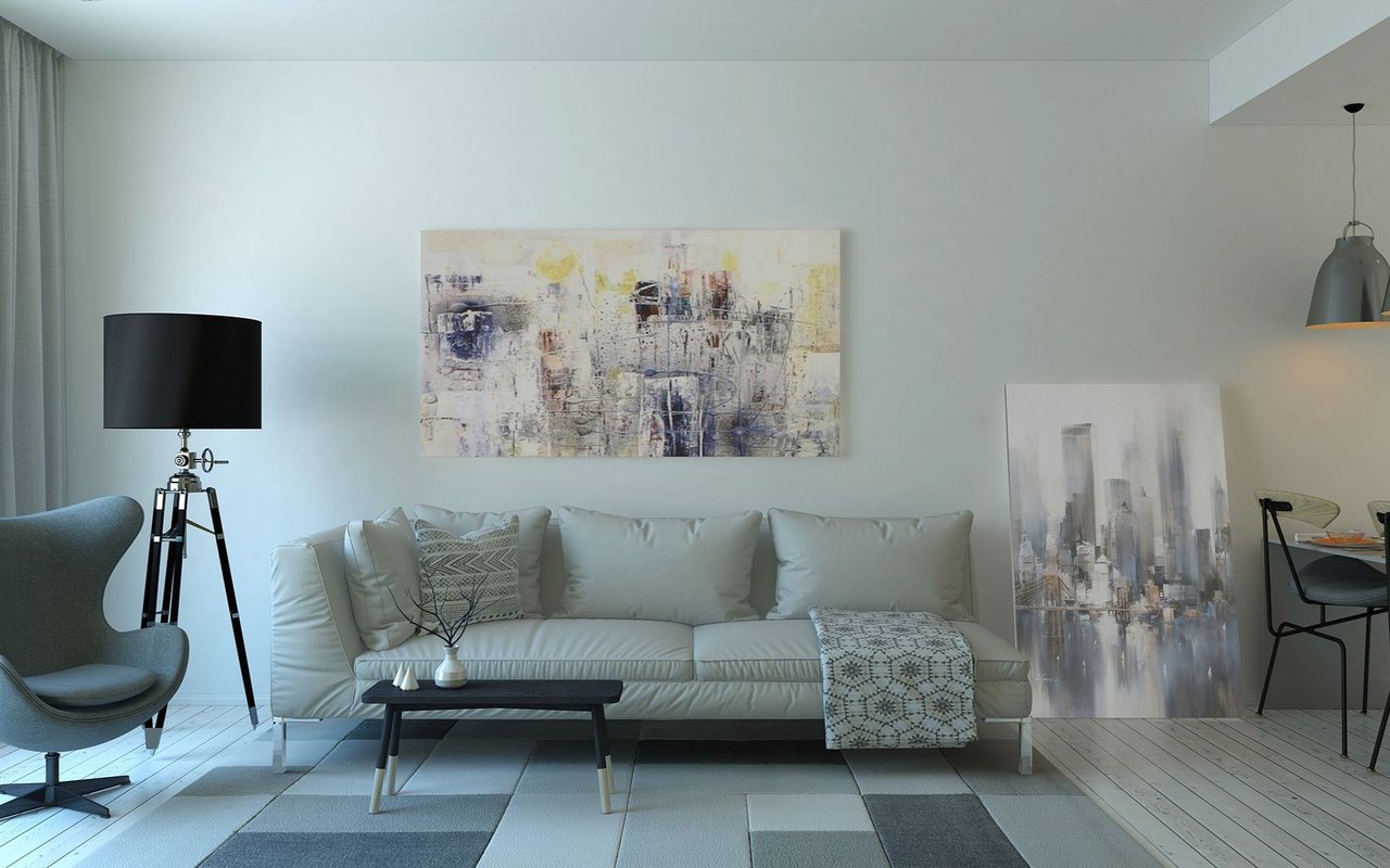 Modern living room with a white sofa, abstract artwork, tripod floor lamp, and patterned throw.