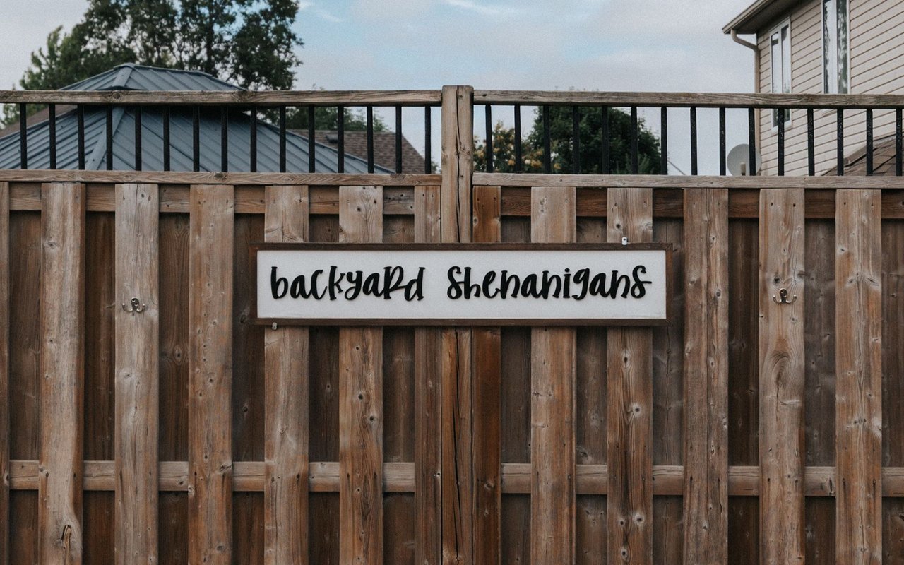 Wooden backyard fence with a sign reading “backyard shenanigans.”