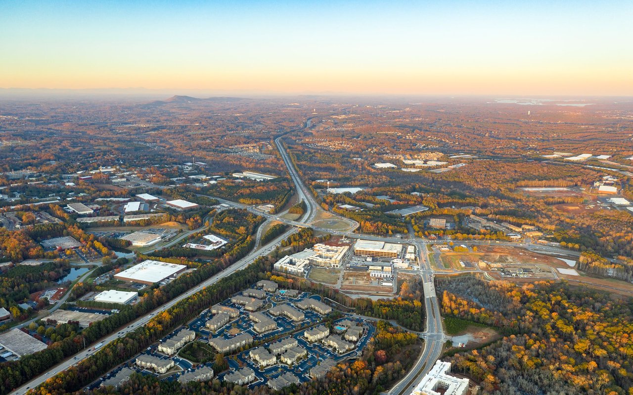 Aerial view of highways, wooded neighborhoods, commercial buildings, and construction in autumn light.