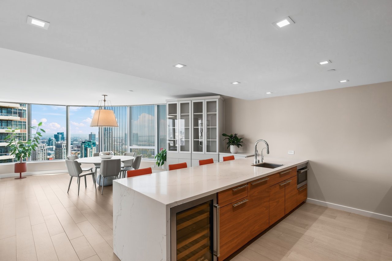 Modern condo kitchen with a long stone island and city skyline views through floor-to-ceiling windows.