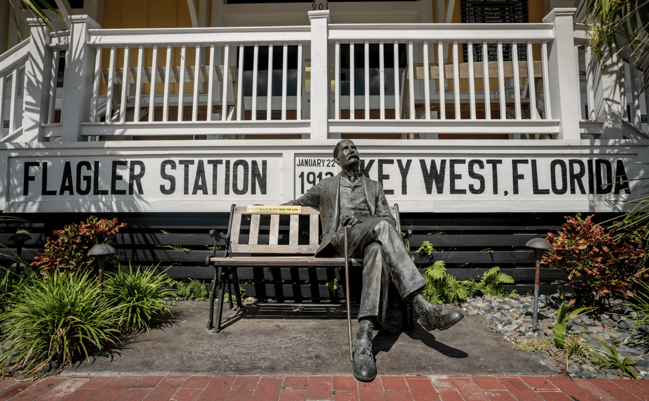 Bronze statue seated outside Flagler Station in Key West, in front of its large station sign.