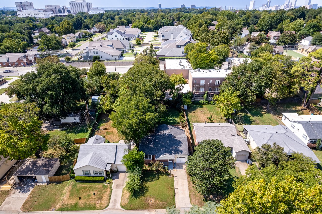 Aerial view of a leafy neighborhood with detached homes and a distant city skyline.
