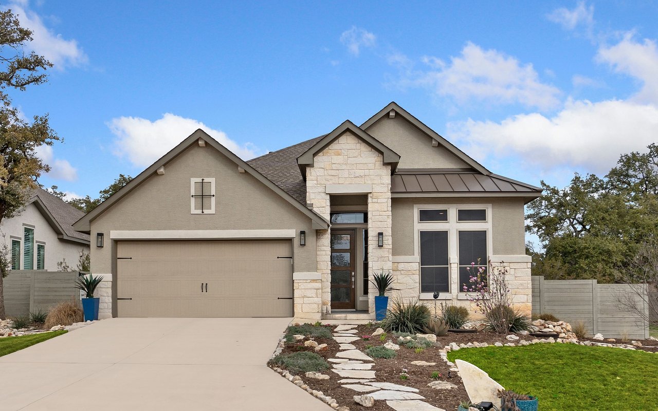 Beige stucco and stone house with a two-car garage and landscaped front walkway.