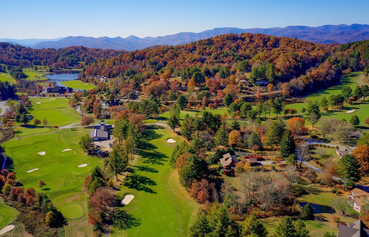 Aerial view of a golf course community amid autumn-colored hills and distant mountains.