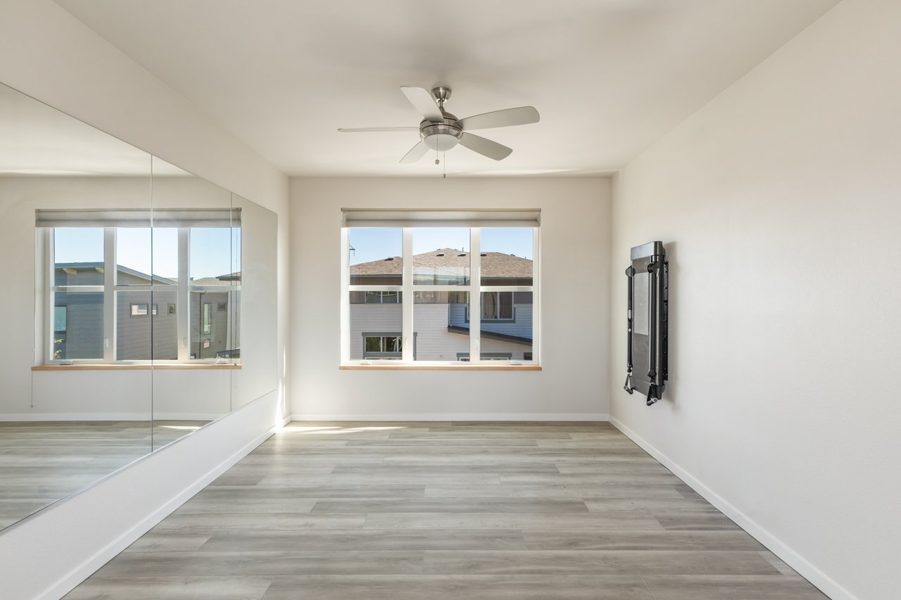 Open loft with a ceiling fan, two windows, and a mirrored wall