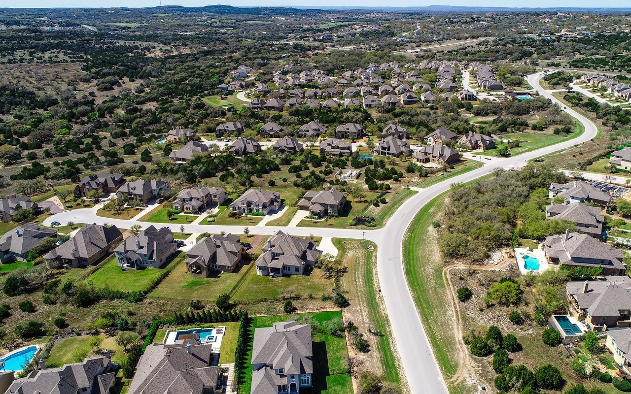 Aerial view of a suburban neighborhood with a winding road, swimming pools, and wooded hills.