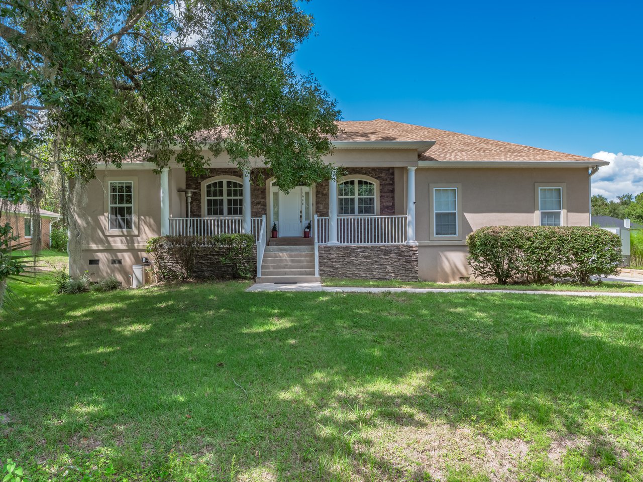 Single-story home with a stone-accented entry, covered porch, and tree-shaded lawn.