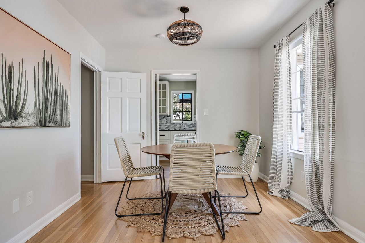 Dining room with a wooden table, woven chairs, hardwood floors, and a view into the kitchen.