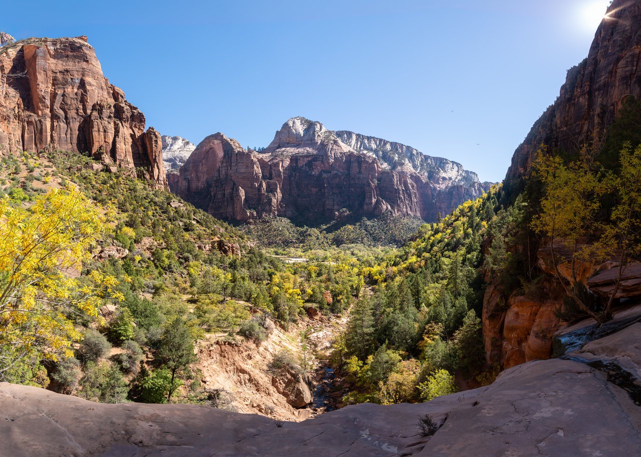 Red sandstone canyon framed by steep cliffs and yellow autumn foliage.