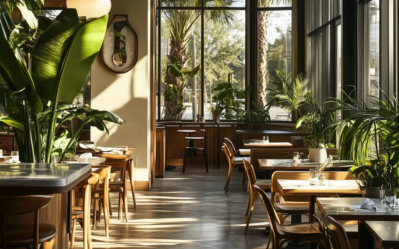 Sunlit restaurant interior with wooden tables and lush green plants