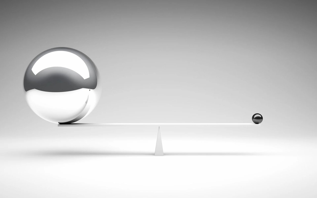 A balance beam weighs a large sphere against a tiny one.