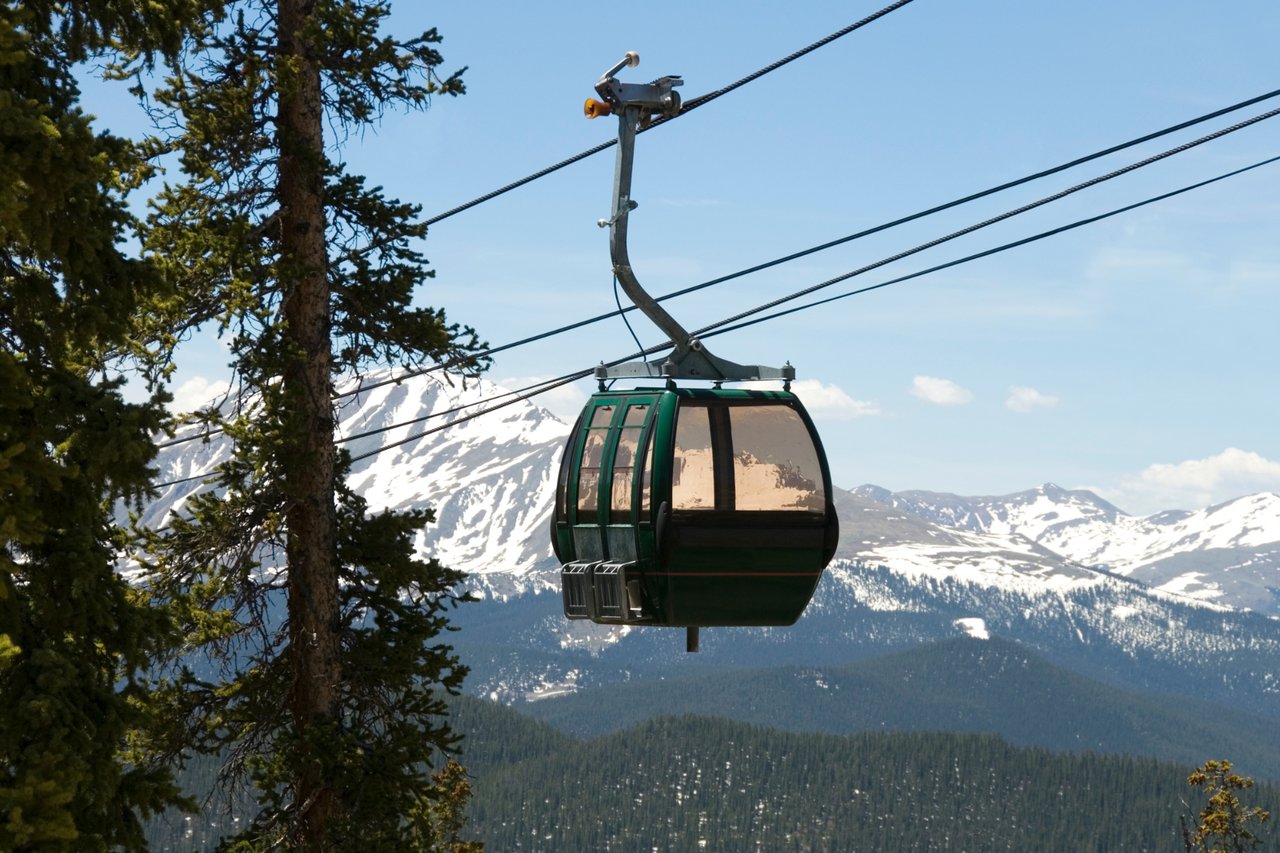 Gondola over a forested mountain valley with snow-covered peaks in the background.