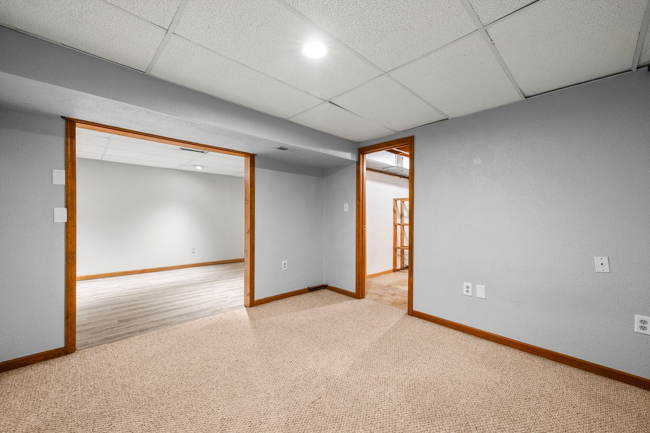 Empty carpeted room with gray walls and wood trim, opening to two adjoining rooms.