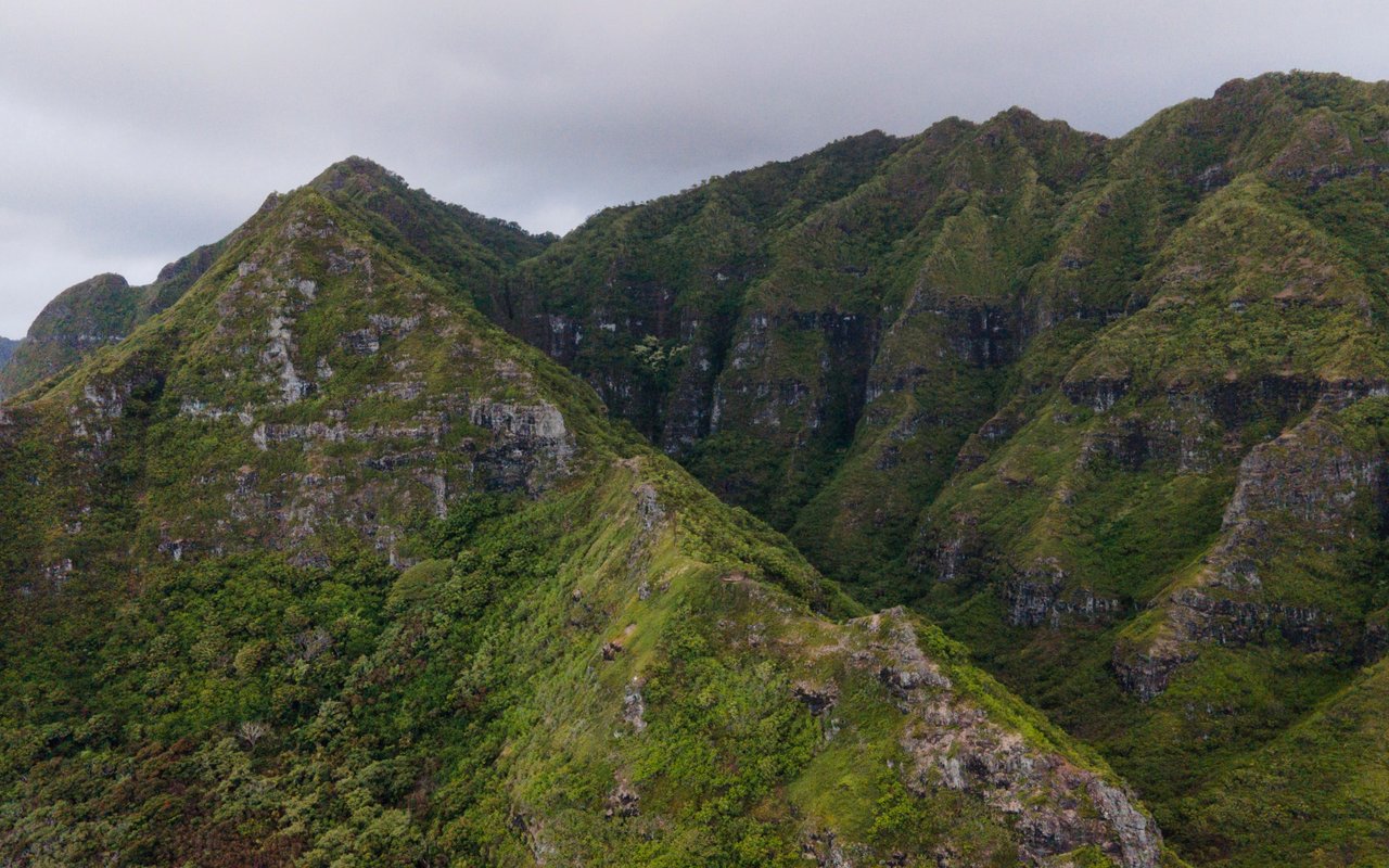 Lush mountain ridges with rocky cliffs beneath an overcast sky.