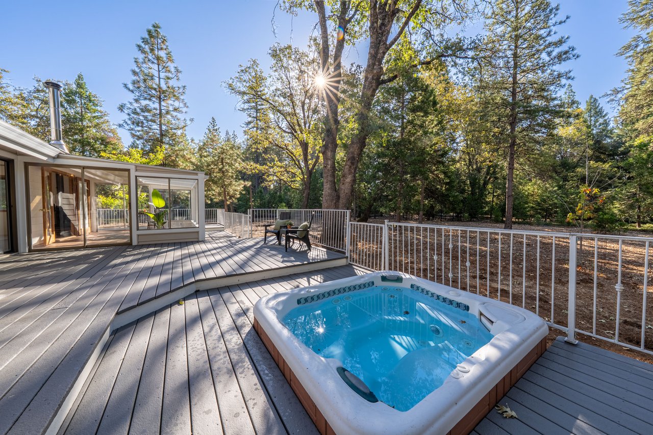 Wooden deck with a hot tub, white railings, and mature trees surrounding the yard.