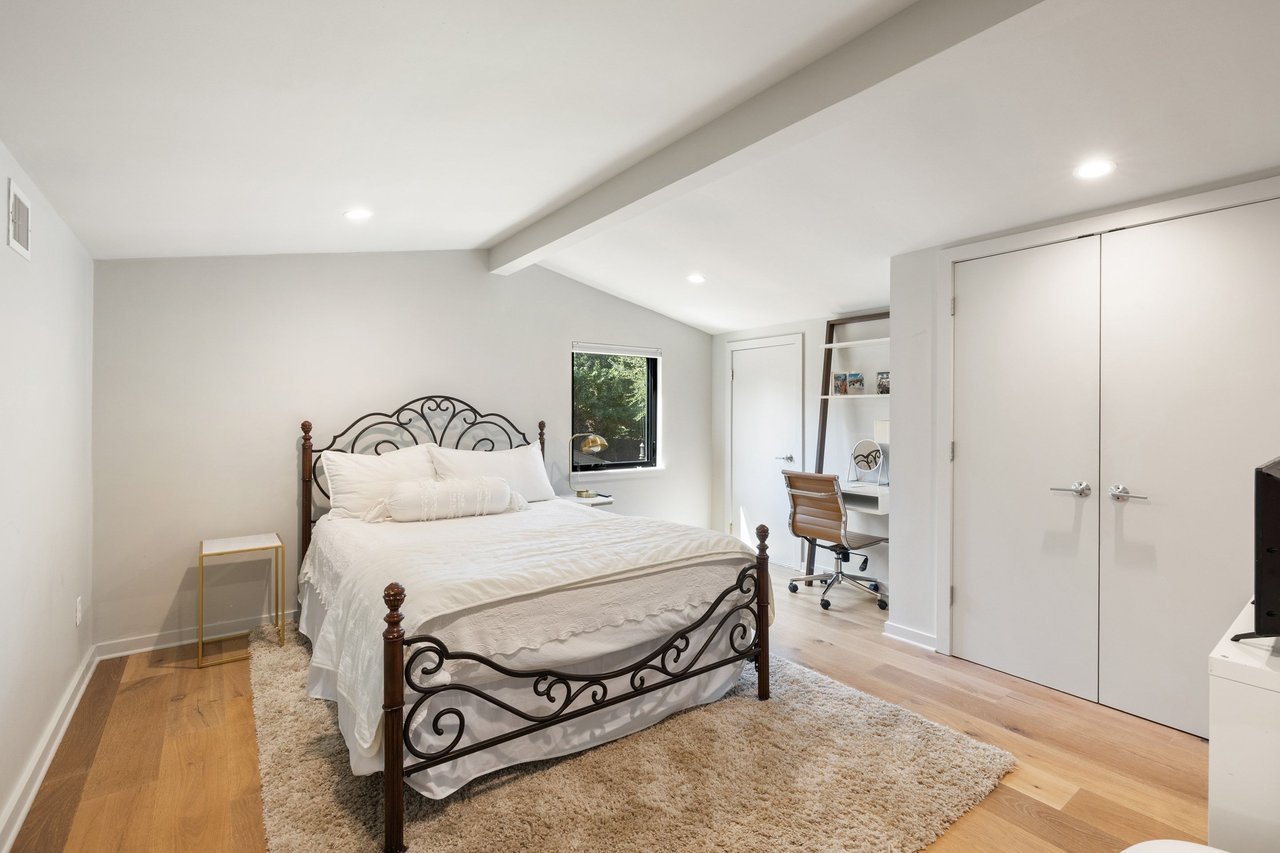 Bedroom with an ornate metal bed, built-in desk nook, and double closet doors.