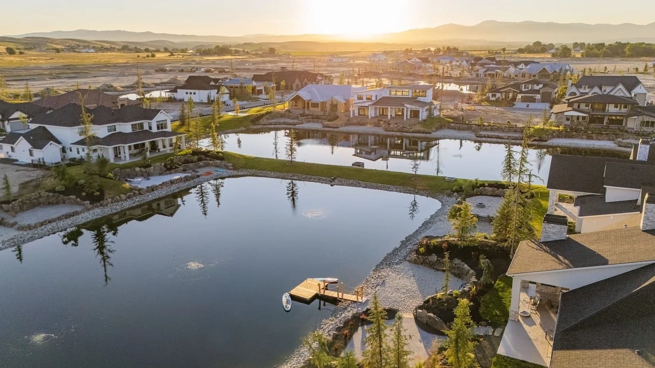 Aerial neighborhood with ponds, a small dock, and distant mountains at sunset.
