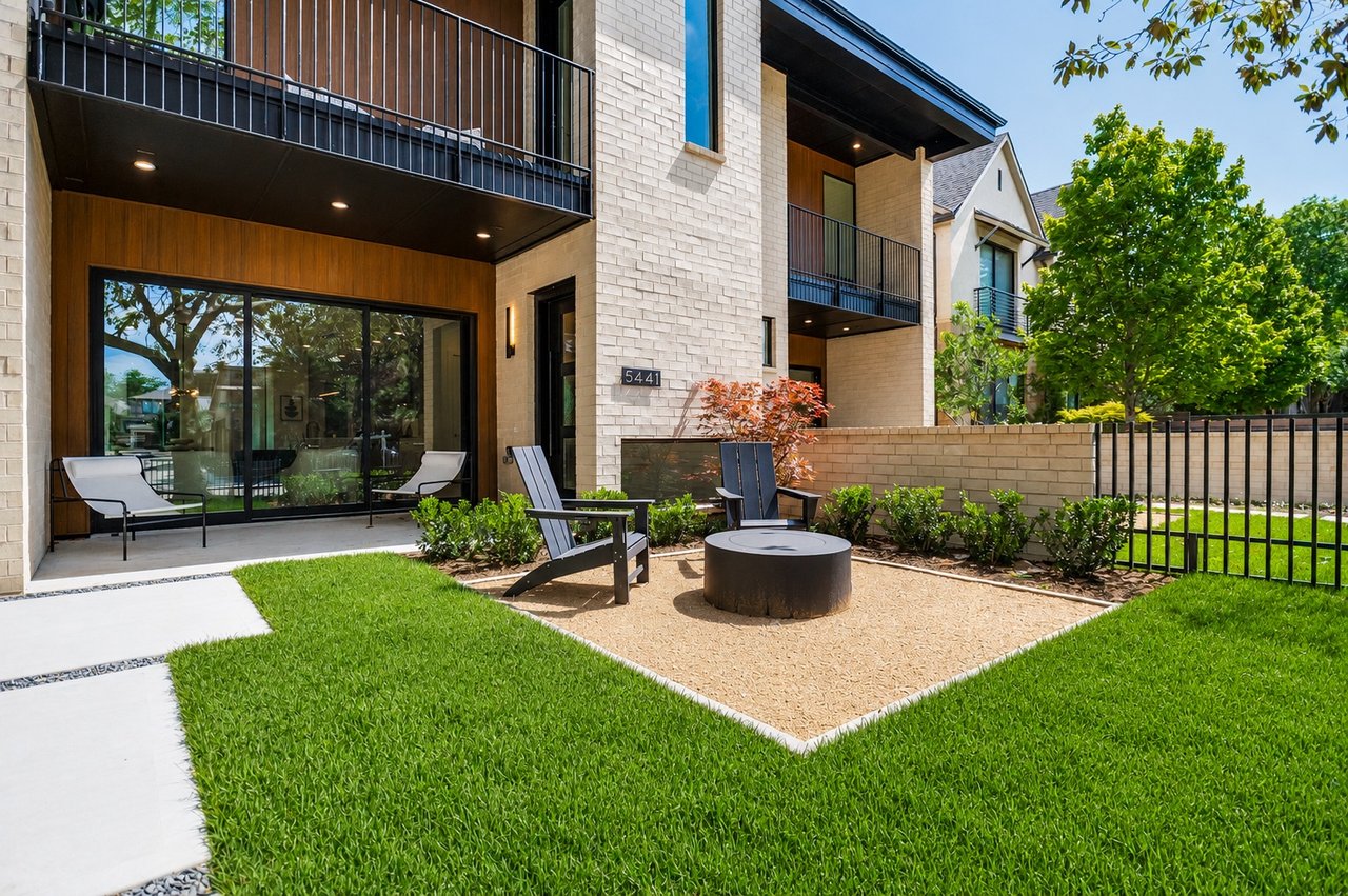 Modern brick residences with dark balconies beside a lawn and shared patio with chairs and a fire pit.
