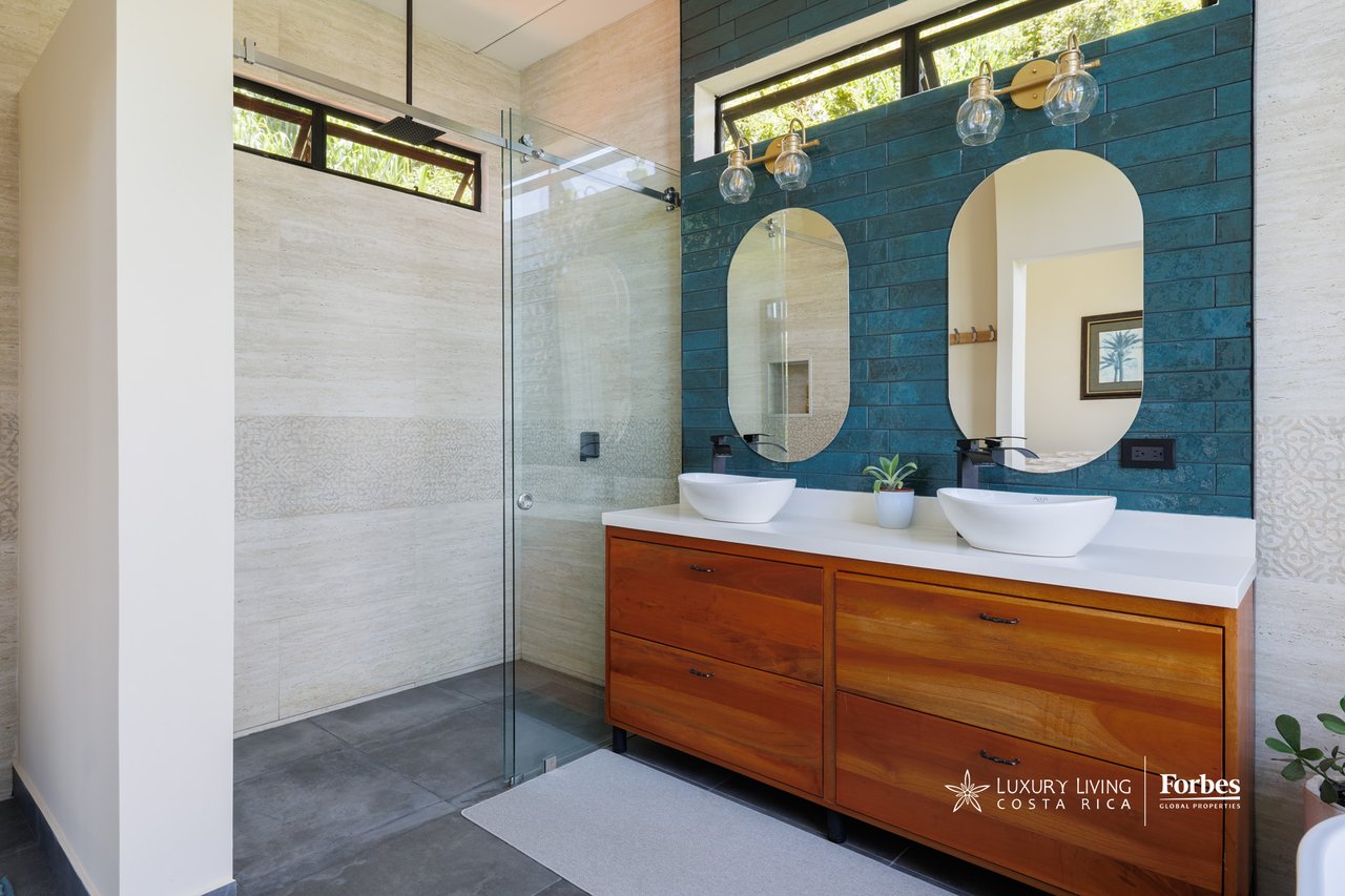 Modern bathroom with a glass shower, double vessel sinks, wood vanity, and teal tiled accent wall.