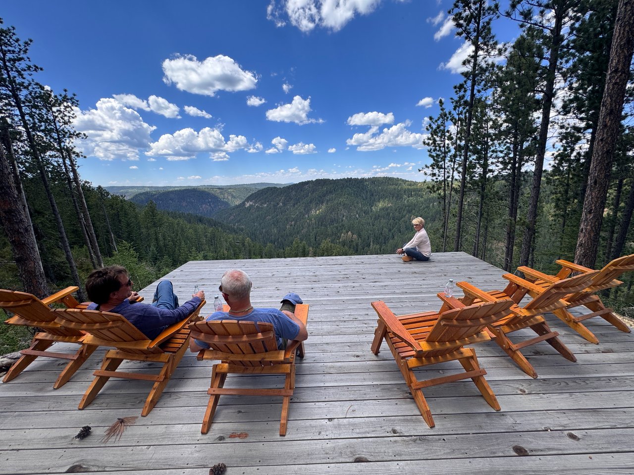 Homeowners relaxing in Adirondack chairs on a private wooden summit deck overlooking a vast mountain canyon.
