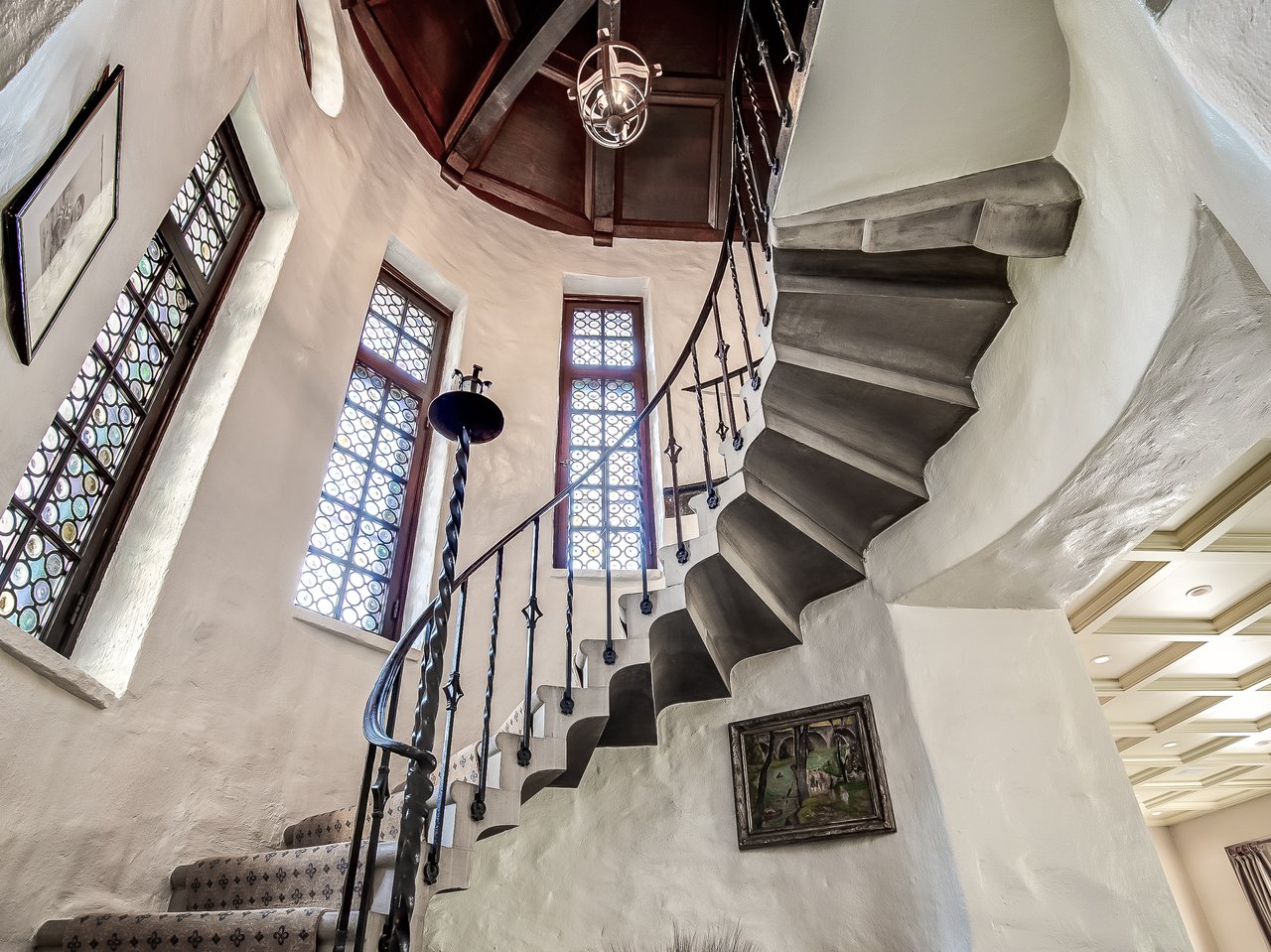 Curving staircase with wrought-iron railing, stained-glass windows, and a dark timber ceiling.