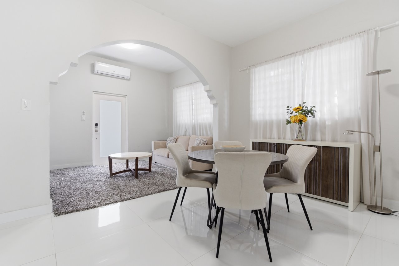 Open-plan living and dining area with a round table, cream furnishings, and an arched opening.