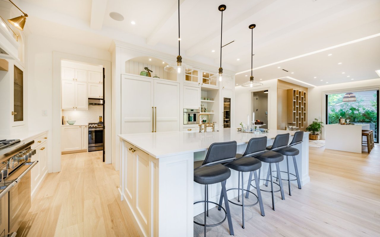 Modern white kitchen with a large island, brass hardware, and four dark bar stools.
