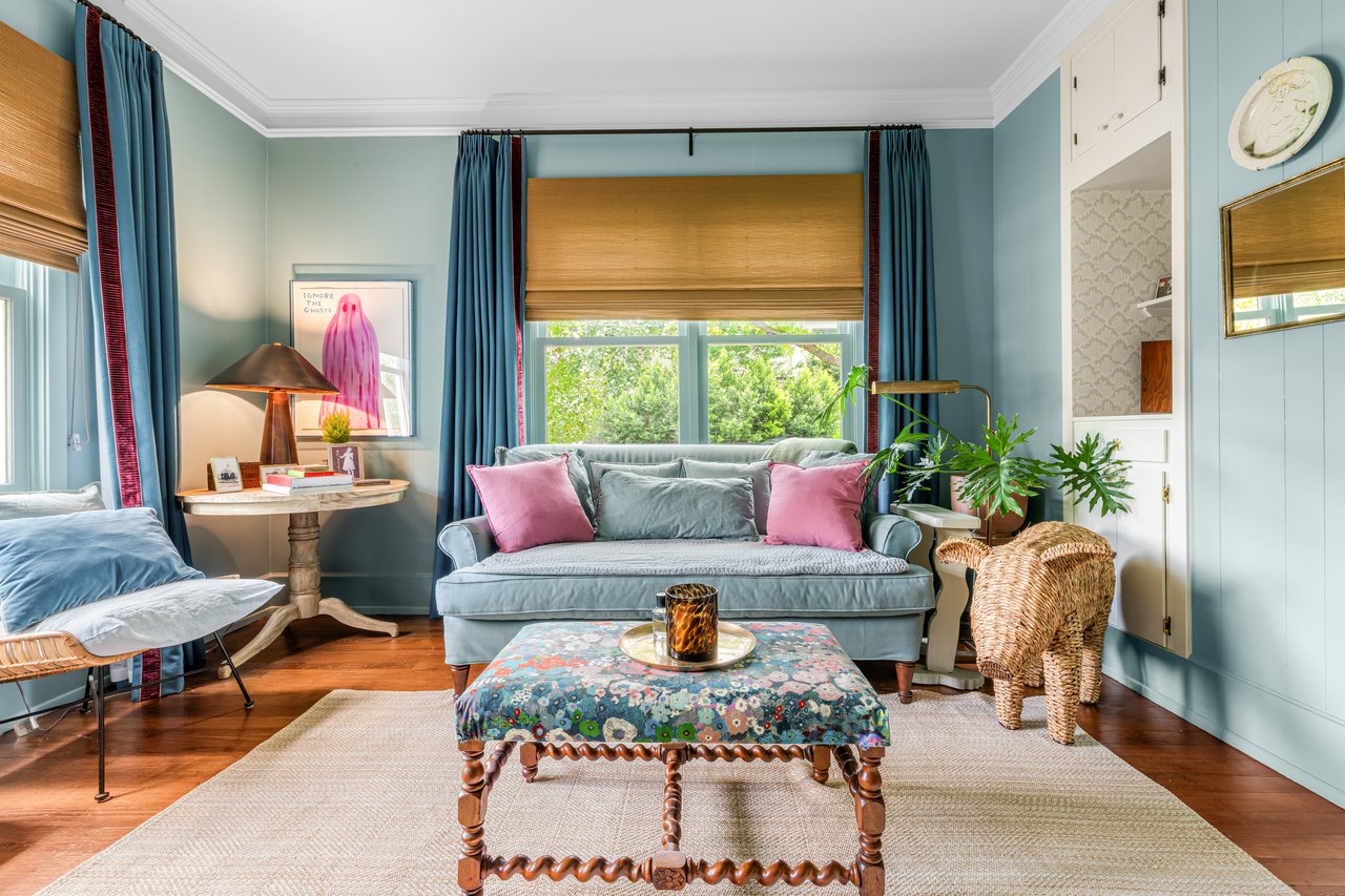 Living room with a gray sofa, pink cushions, blue curtains, and a floral upholstered coffee table.