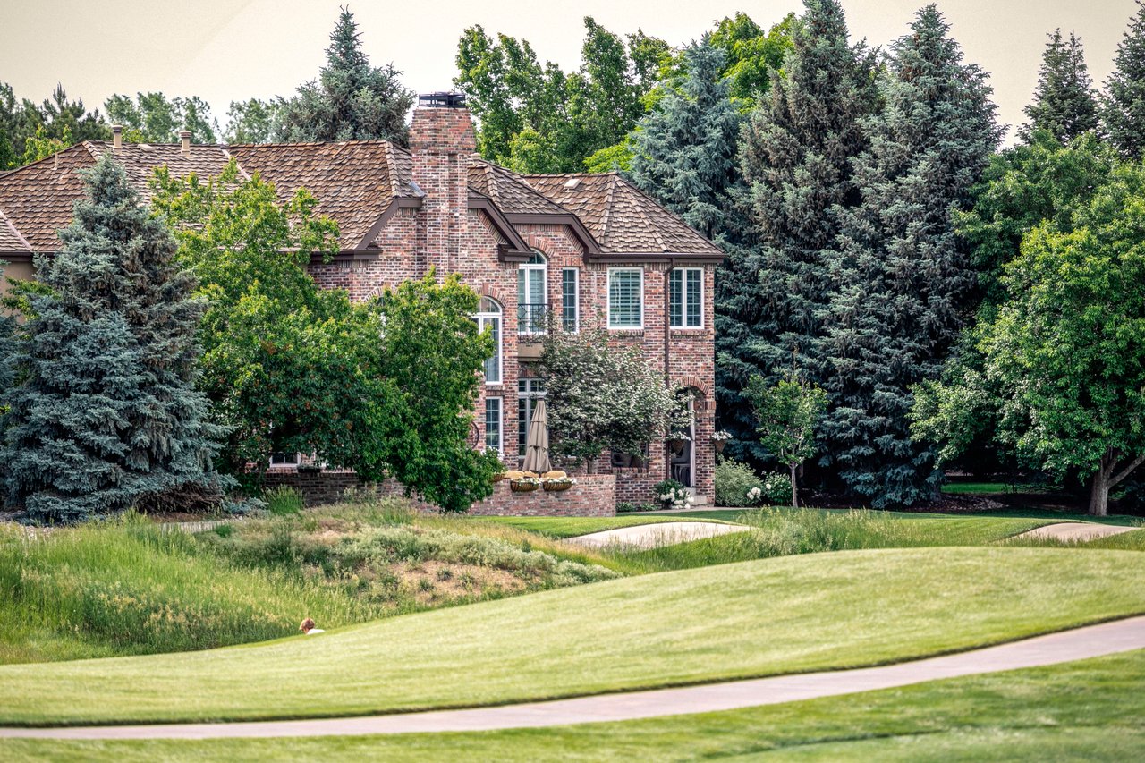 A large brick house with a red door surrounded by tall trees.