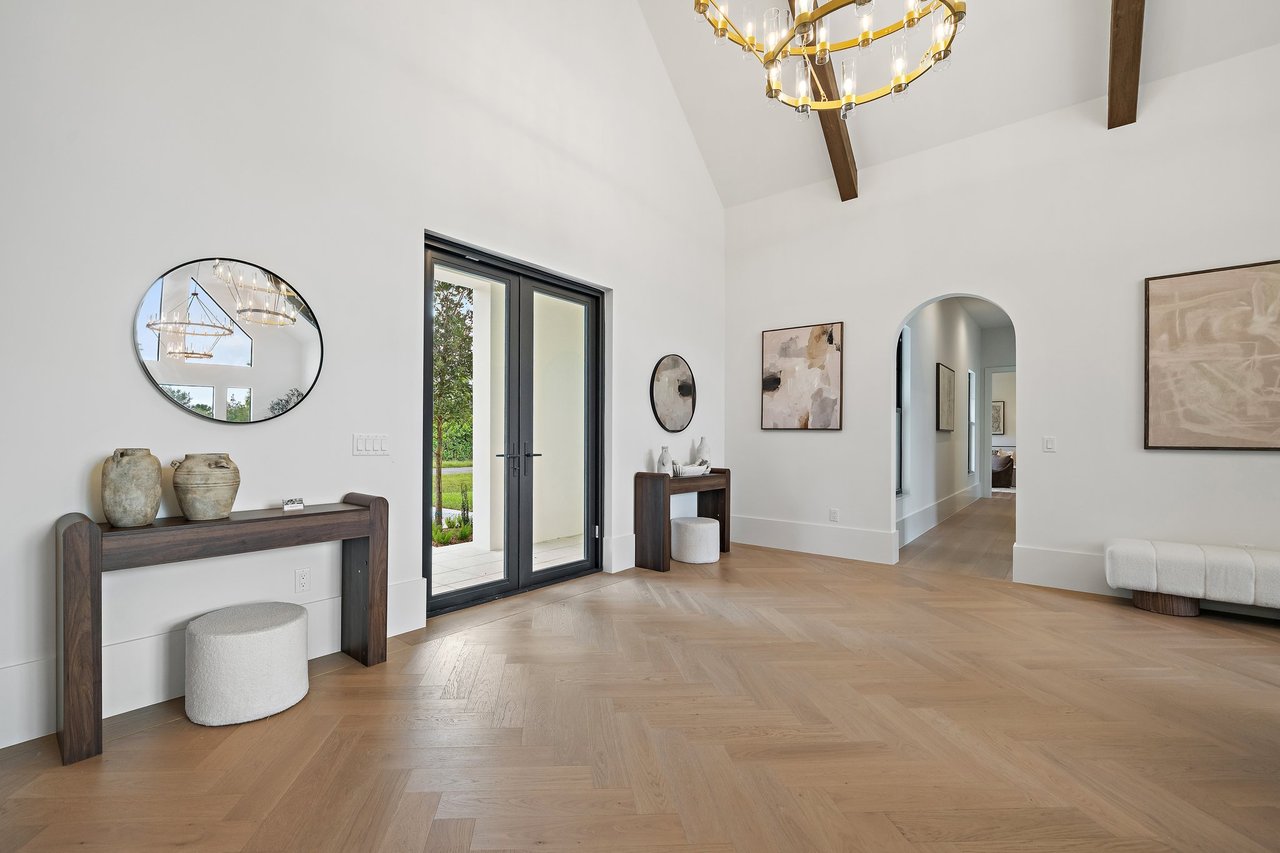 Entry foyer with vaulted ceiling, glass doors, gold chandelier, and herringbone wood floors.