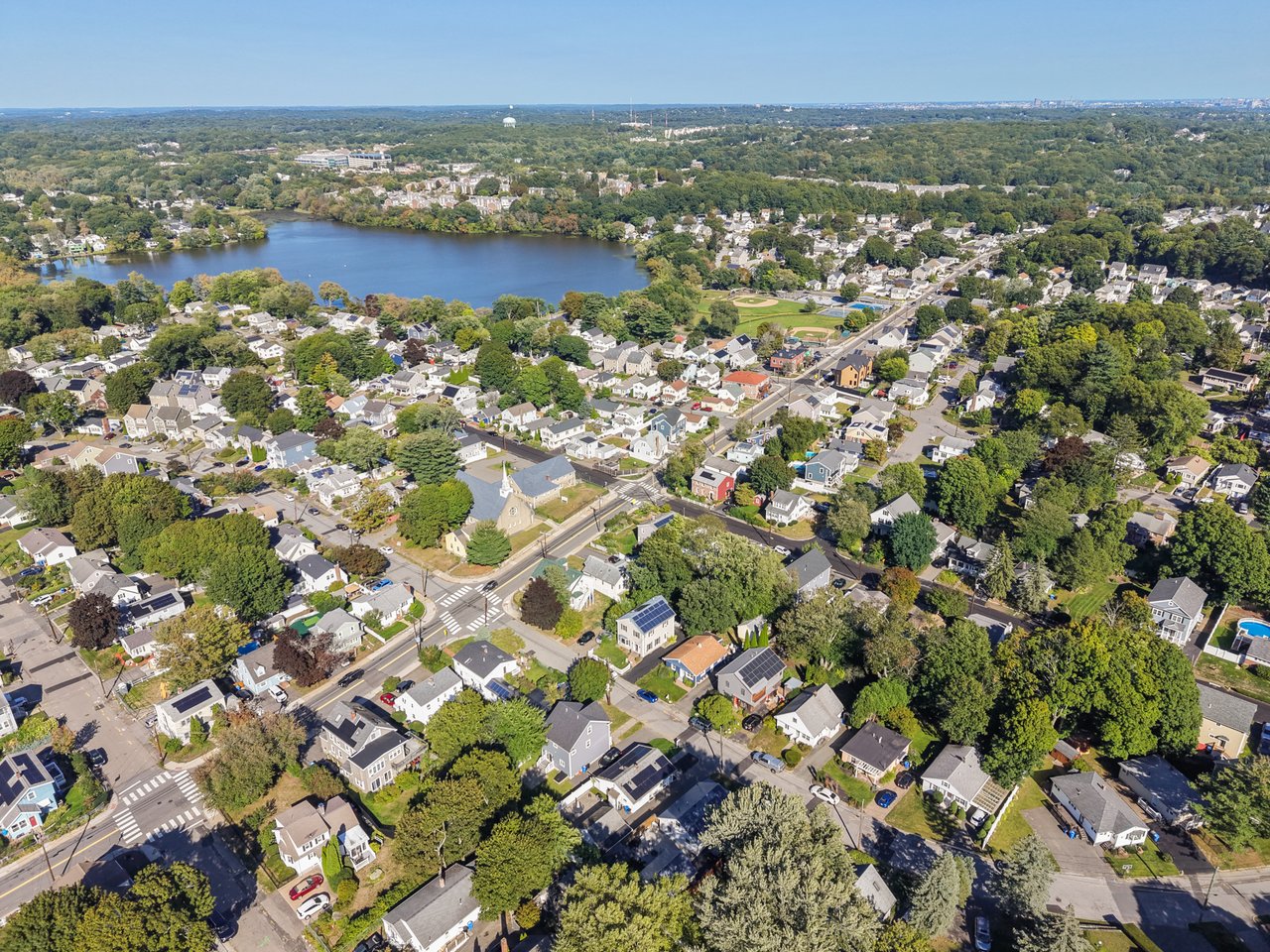 Aerial view of a tree-lined neighborhood surrounding a lake, with streets and a baseball field.