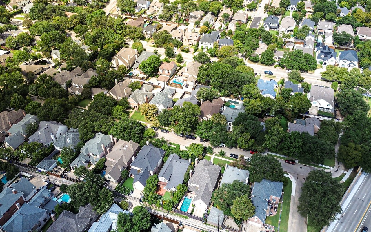 Aerial view of a leafy neighborhood with detached homes, tree-lined streets, and several swimming pools.