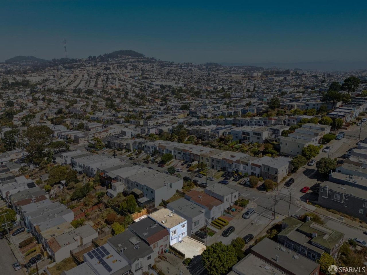 Aerial view of a dense neighborhood with rows of homes and distant hills.