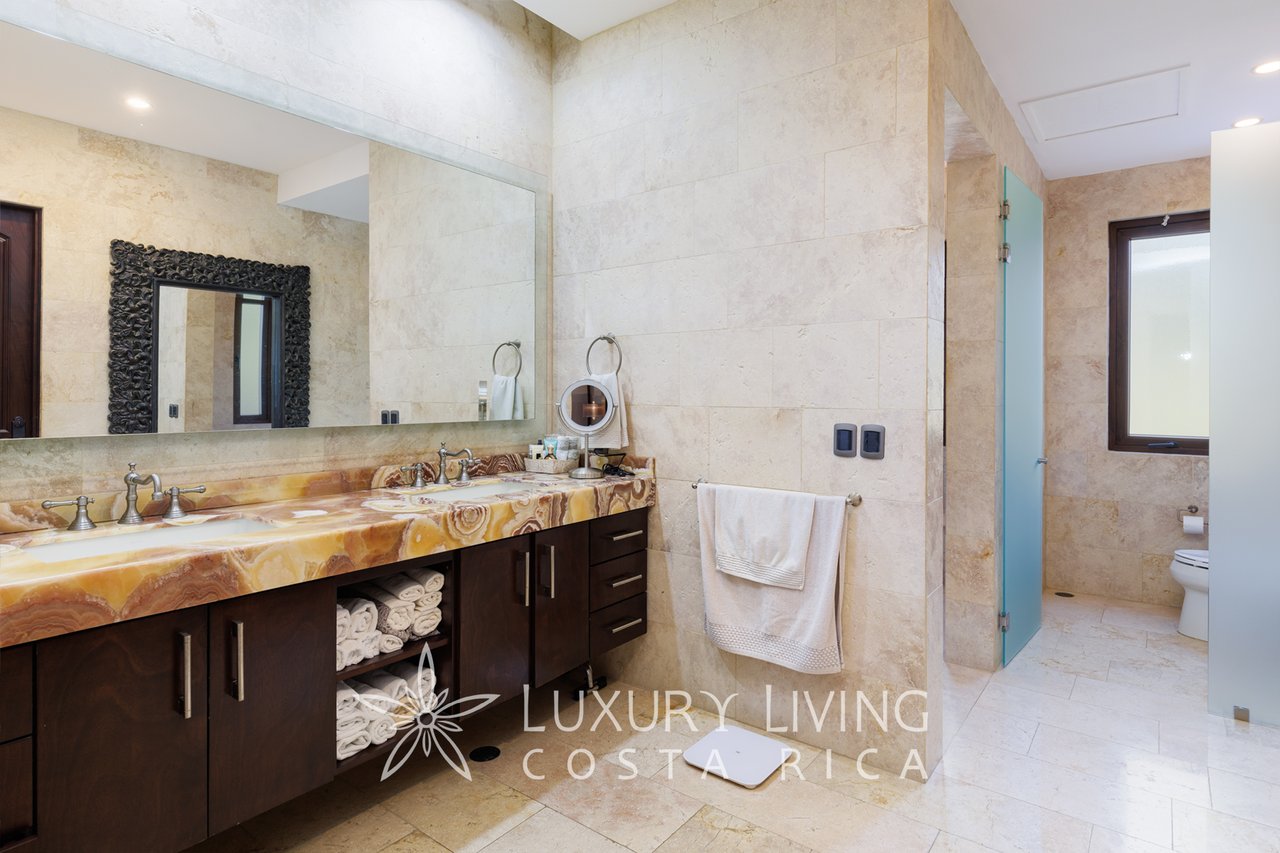 Luxury bathroom with a double vanity, veined stone countertop, dark wood cabinets, and glass shower.