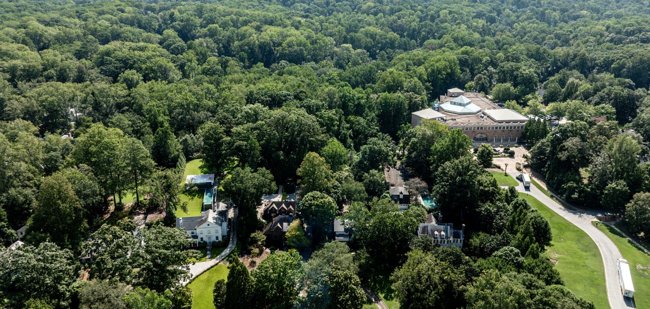 Aerial view of a wooded property with several homes, a pool, and a large building.