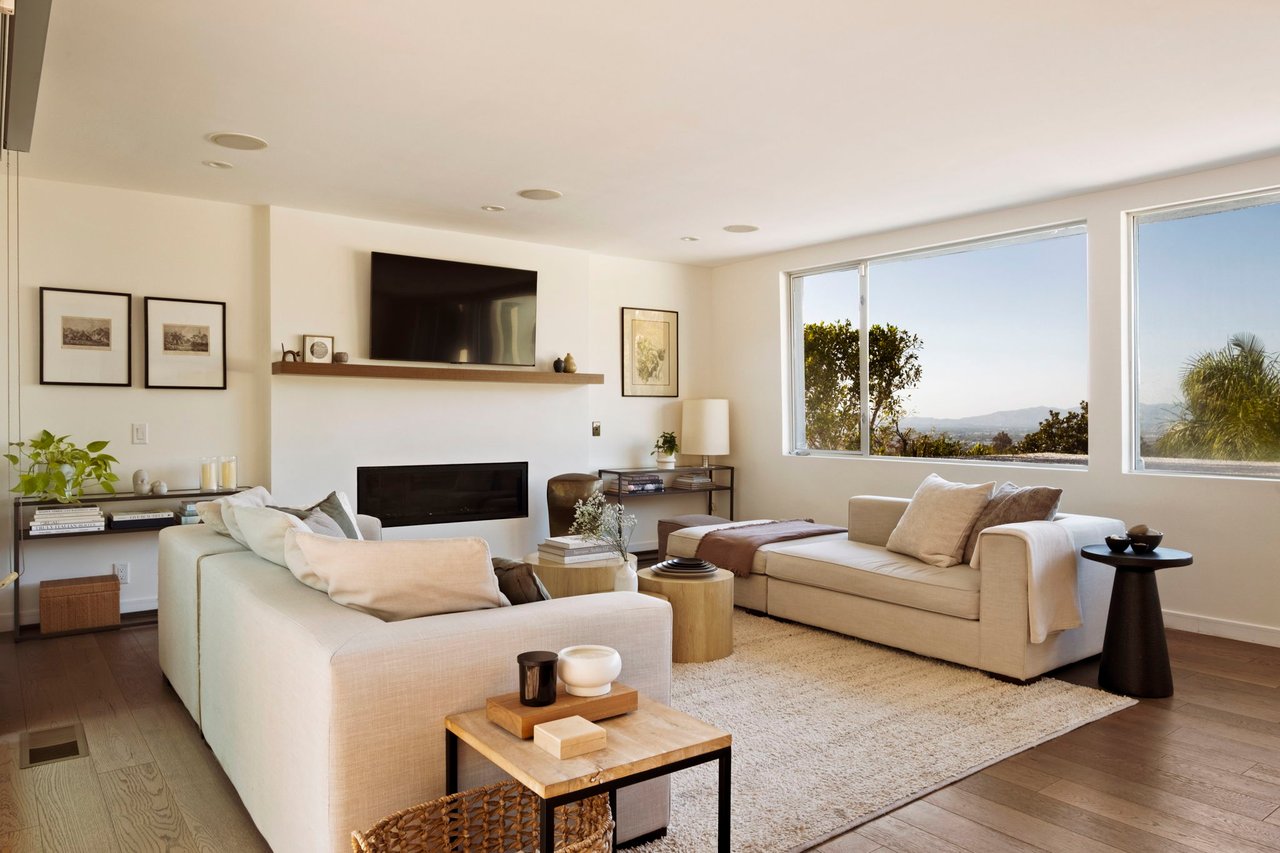 Living room with cream sofas, a fireplace, and large windows overlooking distant hills.