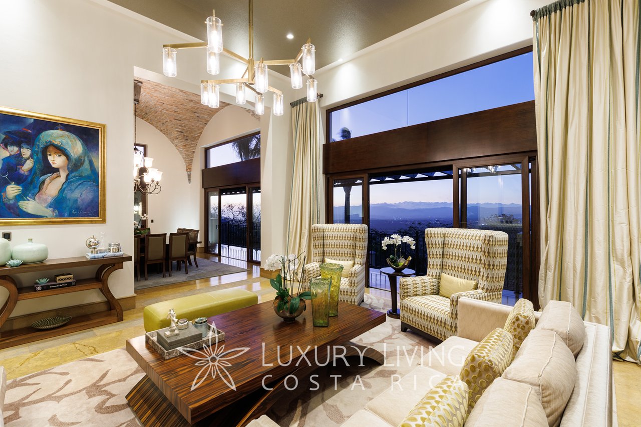 Furnished living room with patterned armchairs, tall windows, and distant mountain views at dusk.