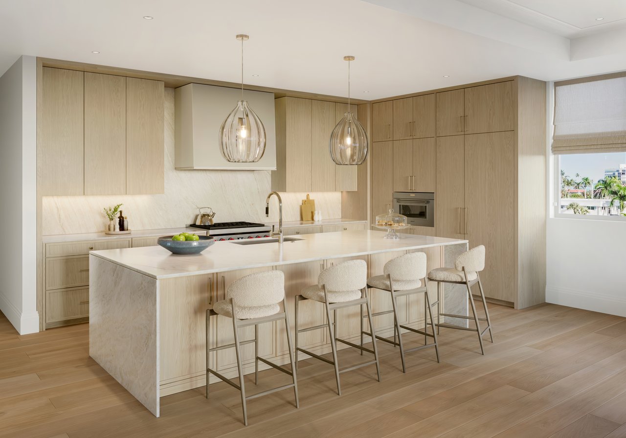Transitional kitchen with a marble island, four upholstered stools, light oak cabinetry, and pendant lights.