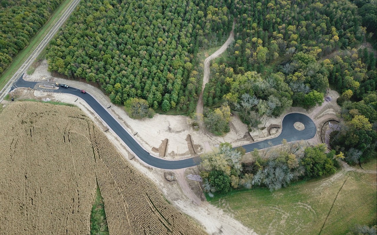 Aerial view of a new curving road and cul-de-sac under construction beside woods and fields.
