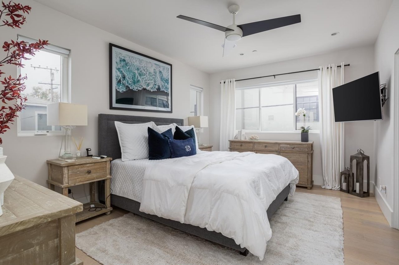  A light and airy bedroom with a gray bed, white bedding, and a large framed artwork of waves above the headboard.