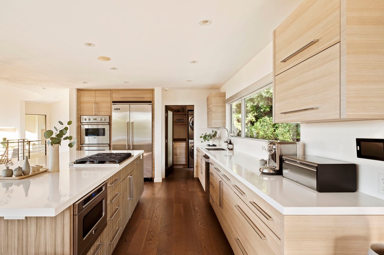 Modern kitchen with light wood cabinets, white counters, stainless steel appliances, and a long island.