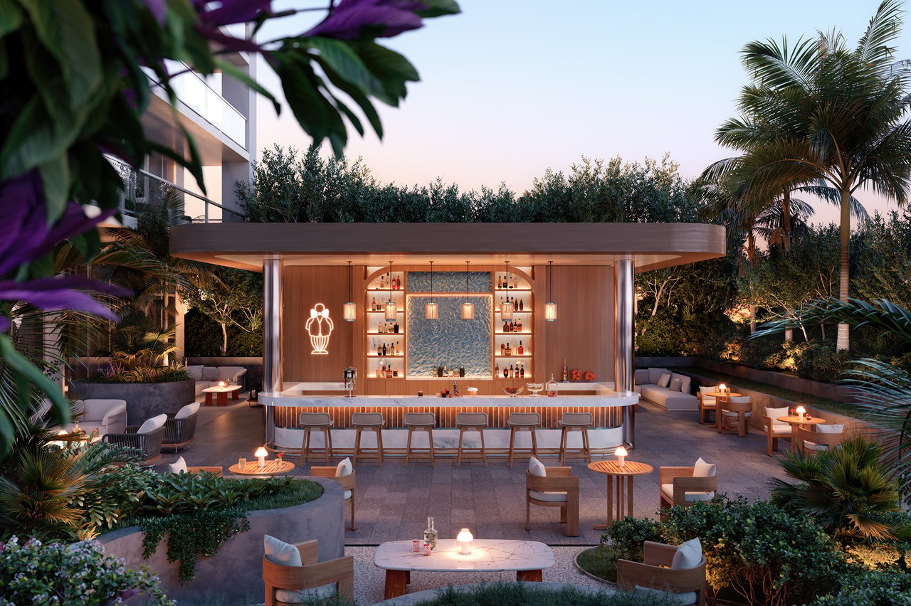 Outdoor bar and lounge terrace with illuminated bar, seating, and tropical landscaping at dusk.