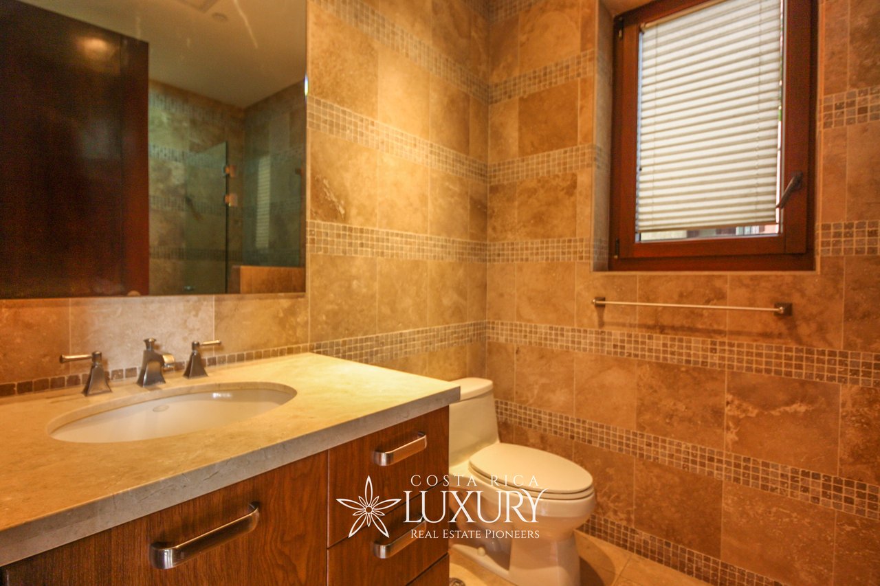 Tiled bathroom with a wood vanity, inset sink, toilet, and shuttered window.